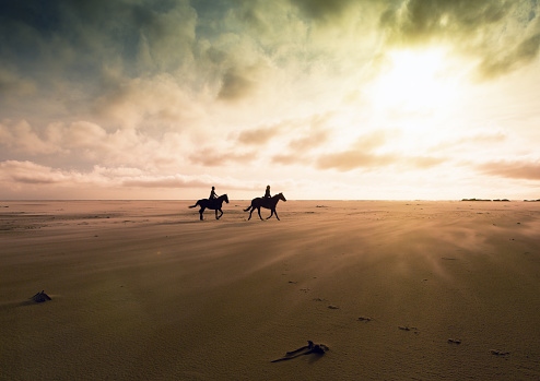 people-horseback-riding-on-the-beach-at-sunset